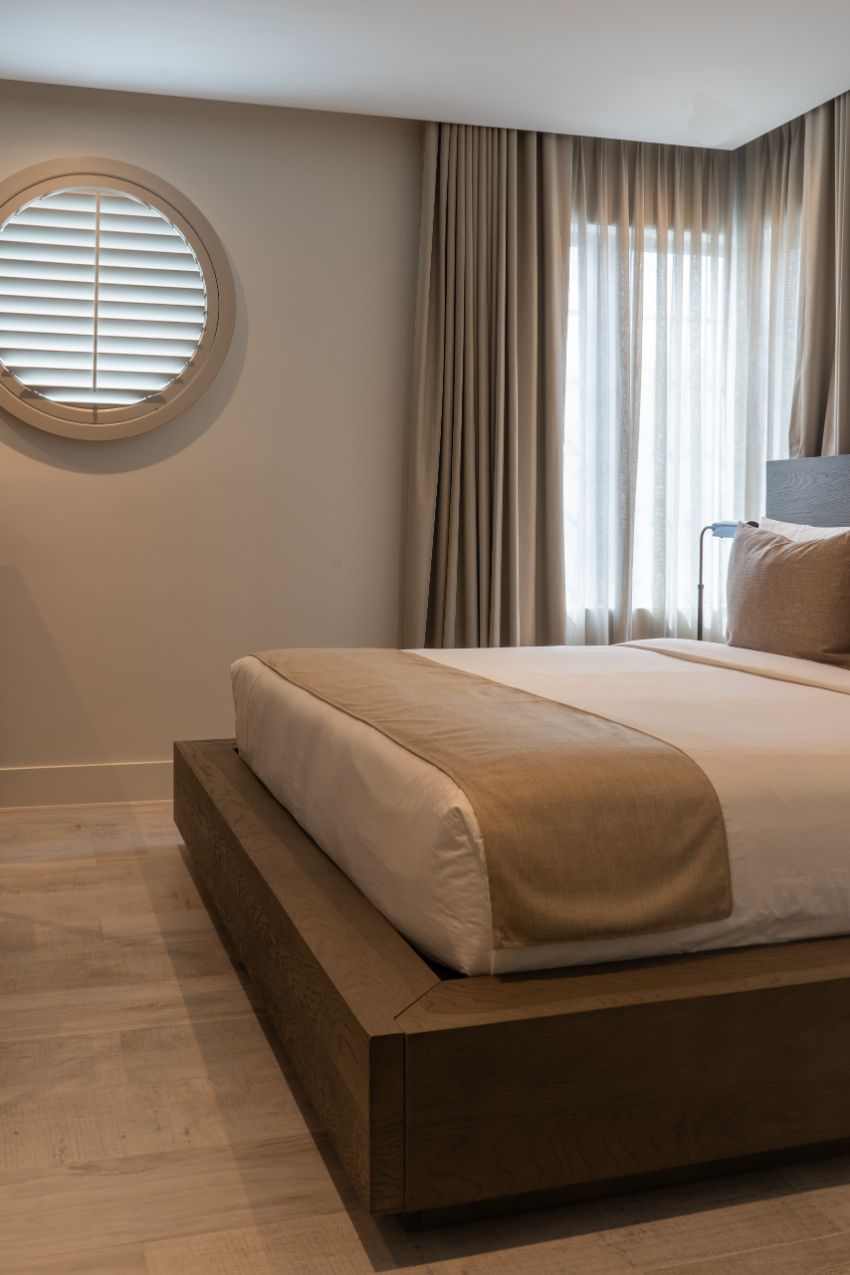 A neatly made bed in a room with a window and curtains.
